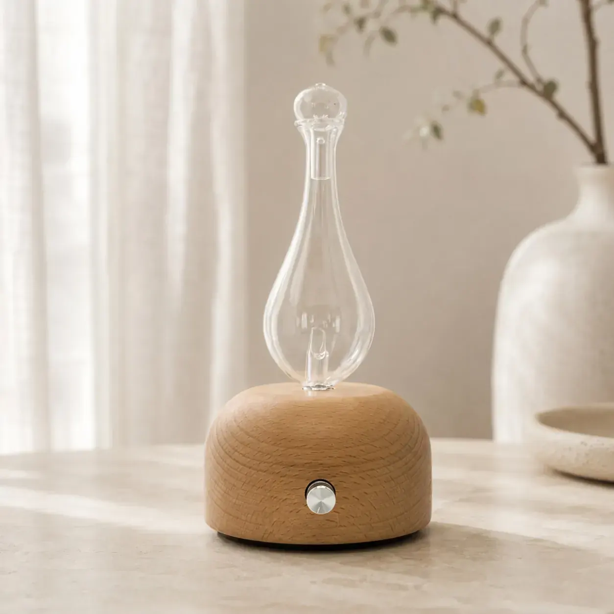 Pear-shaped glass dual-fluid aroma diffuser on a light wood dome base